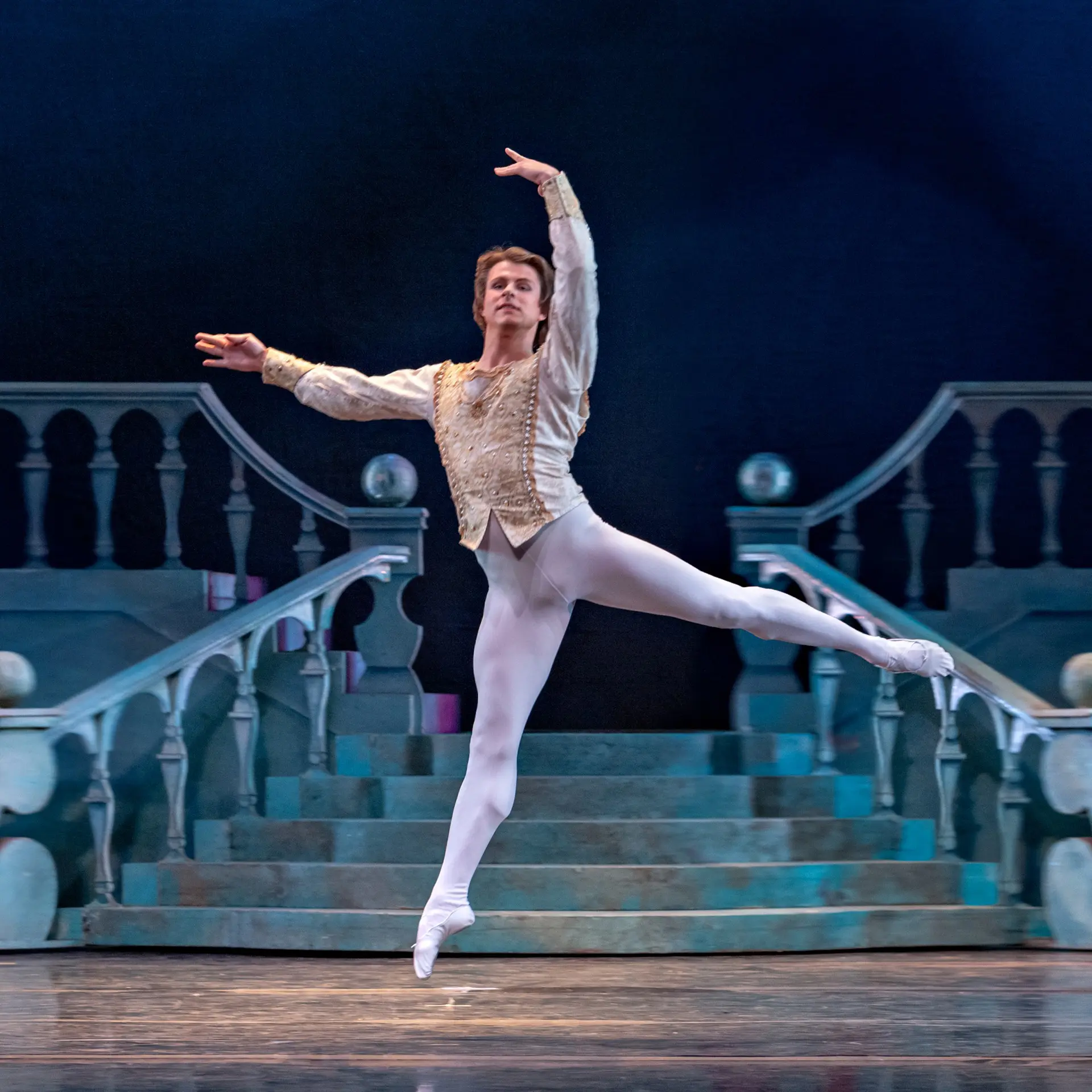 Ballet dancer performing a graceful leap on stage in elegant costume.
