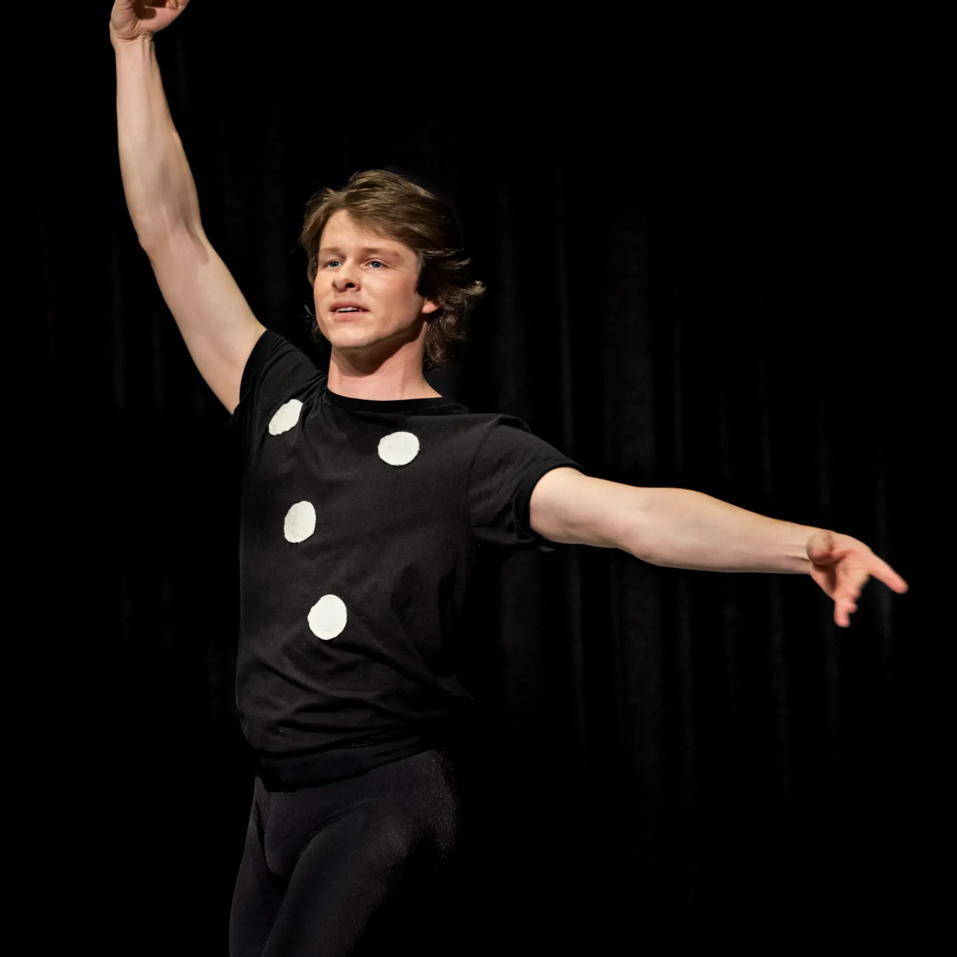 A young dancer in a black shirt with white dots performs on stage.