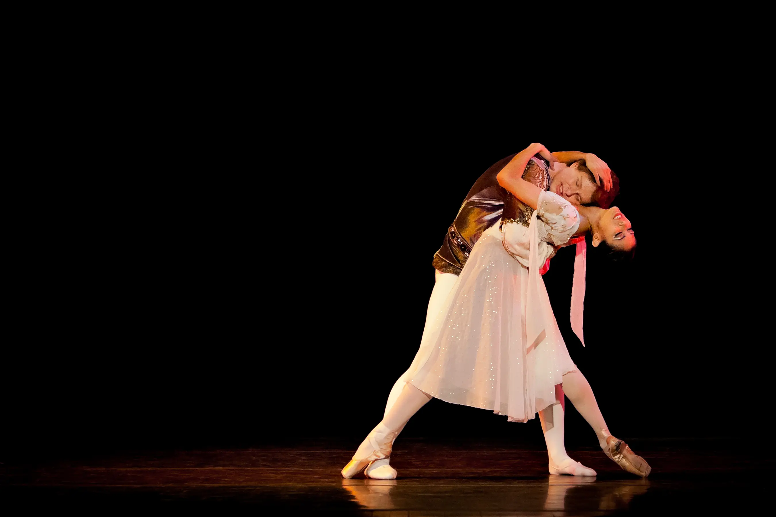 Two ballet dancers performing an elegant pose on stage.