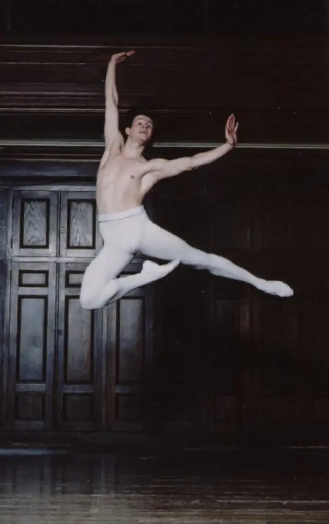 Male ballet dancer performing a grand jeté in a classic setting.