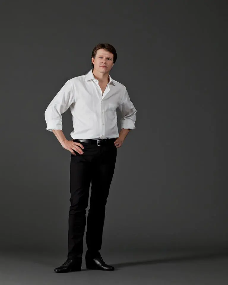 Man in white shirt and black pants posing confidently against a dark background.